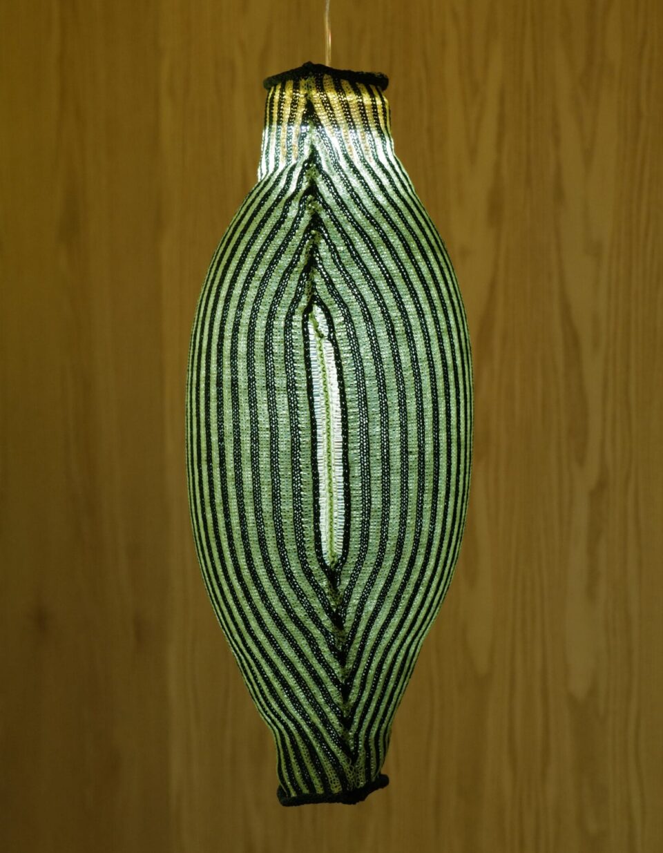 a detail of a suspended greenish-gray textile lamp with vertical stripes