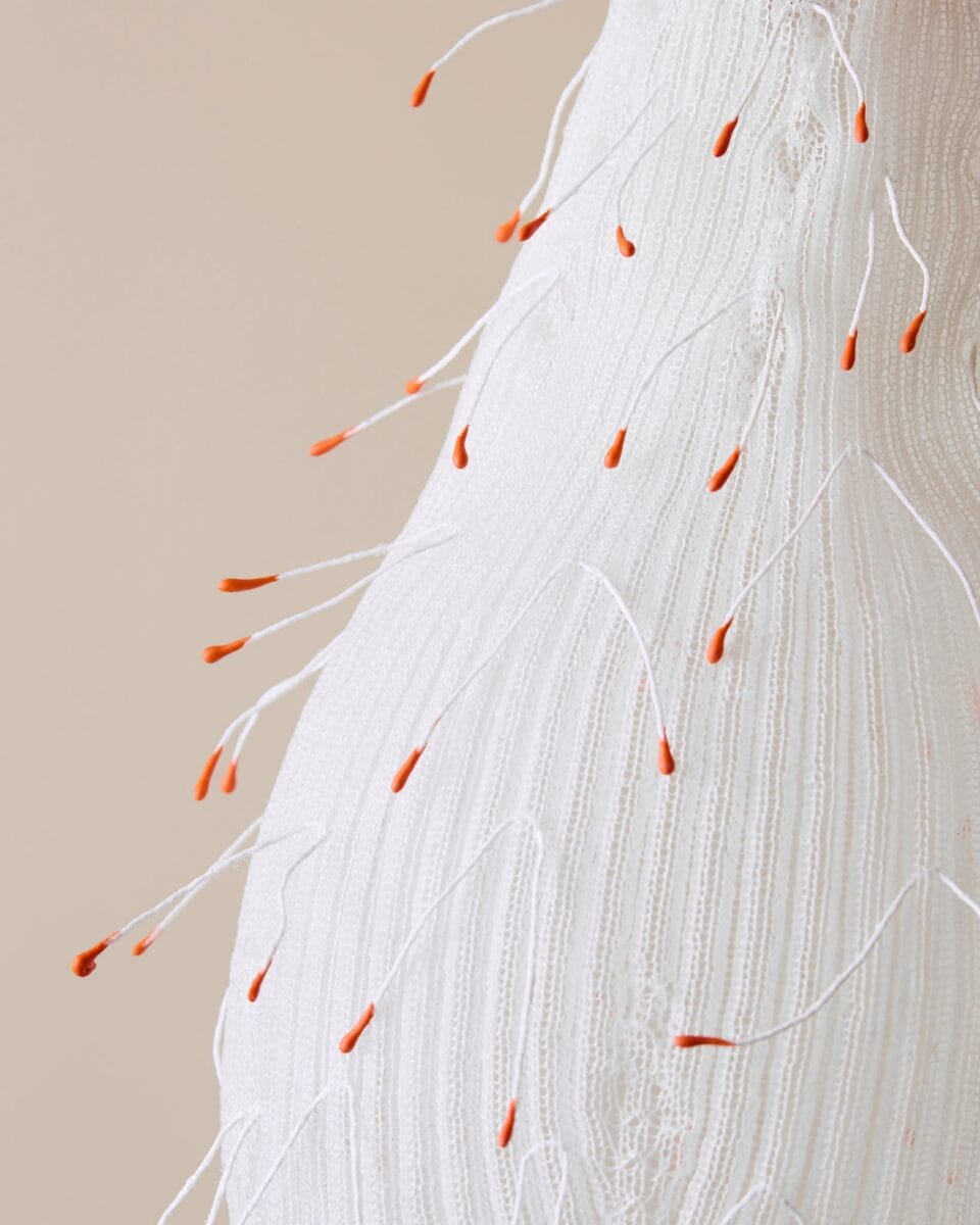 a detail of a suspended white lamp abstractly reminiscent of a fruit with small tendrils on the surface with red tips