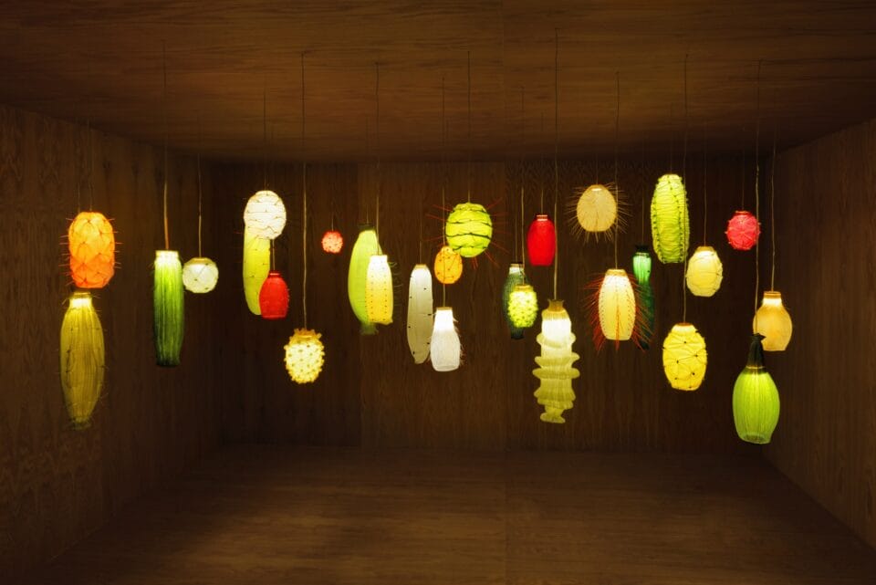 a darkened room with numerous illuminated suspended lights, all loosely reminiscent of tropical fruits