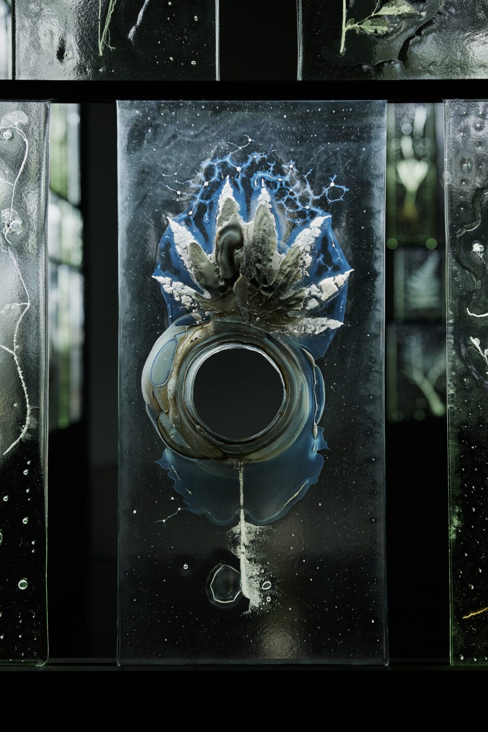 a detail of a multi-paned glass wall sculpture featuring a clear rectangle of solid glass with a frosty impression inside of a plant with bubbles