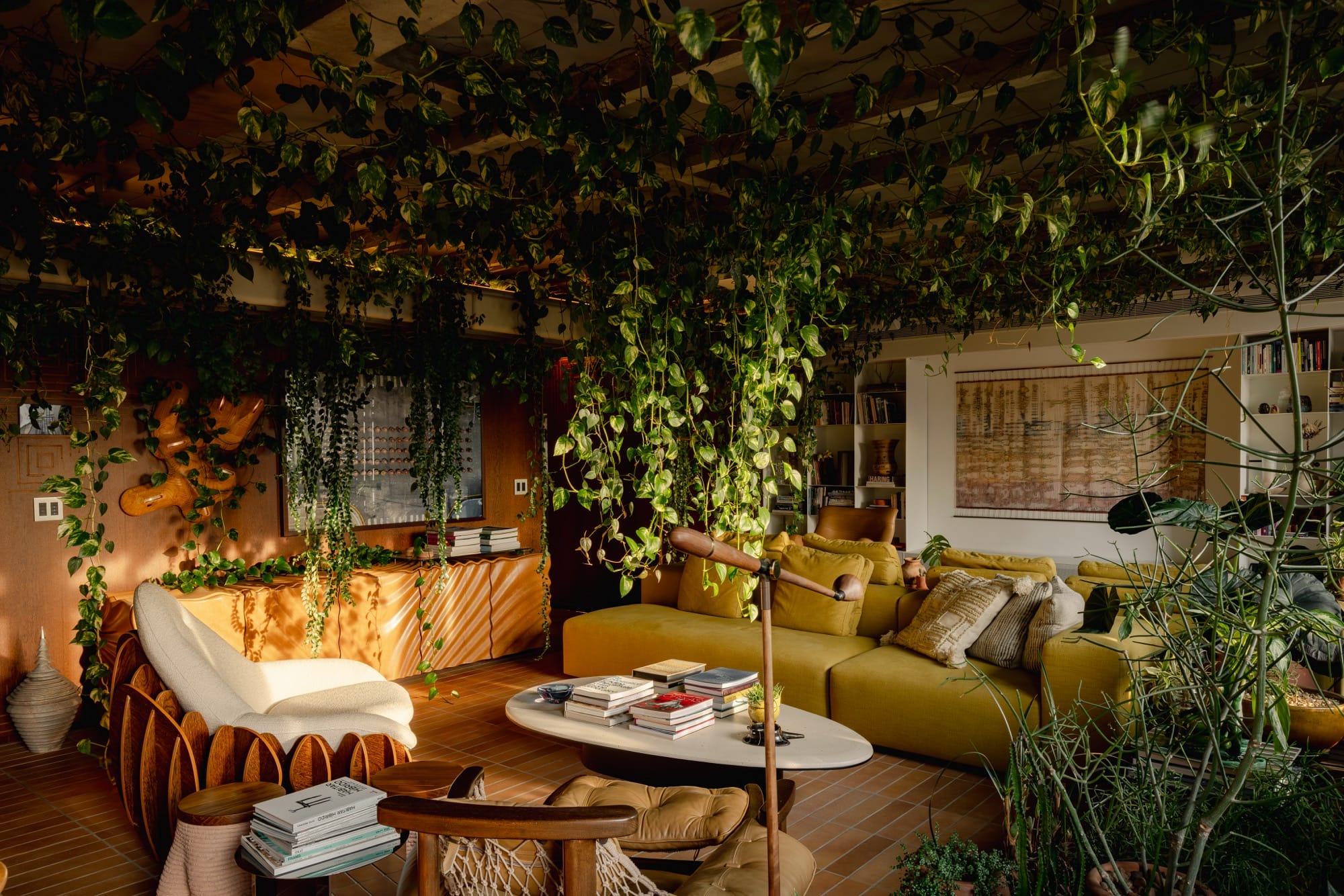 An apartment interior designed by Guto Requena with an eclectic variety of contemporary furnishings and houseplants draping from rafters in the ceiling